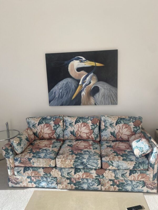 a painting of two great blue herons hanging over a flowered sofa